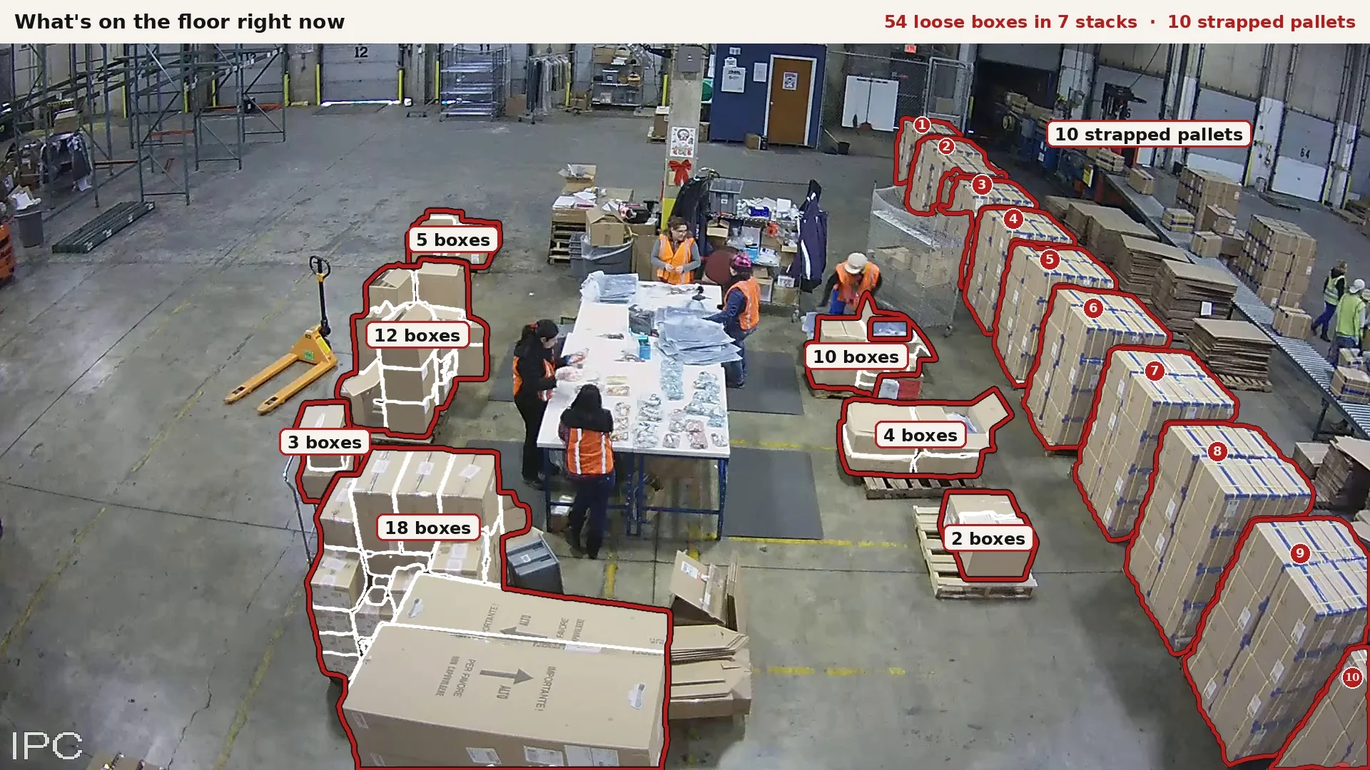 Ceiling camera still of a warehouse floor: 54 loose boxes outlined in 7 stacks and 10 strapped pallets numbered